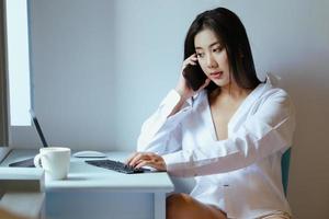The new normal. A businesswoman is using her phone and computer to work for a company. over the Internet on your desk at home. photo
