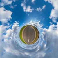 green tiny planet in blue sky with beautiful clouds. Transformation of spherical panorama 360 degrees. Spherical abstract aerial view. Curvature of space. photo