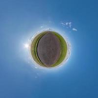 green tiny planet in blue sky with beautiful clouds. Transformation of spherical panorama 360 degrees. Spherical abstract aerial view. Curvature of space. photo