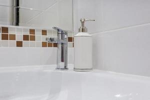 Ceramic Water tap sink with faucet with black soap and shampoo dispensers in expensive bathroom photo