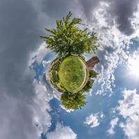 green tiny planet in blue sky with sun and beautiful clouds. Transformation of spherical panorama 360 degrees. Spherical abstract aerial view. Curvature of space. photo