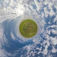 green tiny planet in blue sky with beautiful clouds. Transformation of spherical panorama 360 degrees. Spherical abstract aerial view. Curvature of space. photo