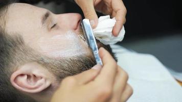 Barber uses straight razor to shave man's neck and face to shape facial hair video