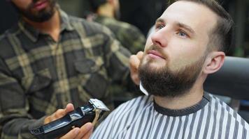 Barber uses electric trimmers to shape man's facial hair video
