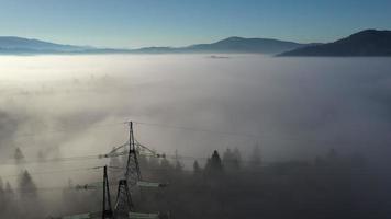 bomen en elektrisch torens top uit van een dicht ochtend- mist in de Karpaten bergen in Oekraïne onder een helder blauw lucht video