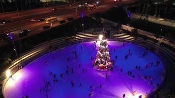 People ice skate around a Christmas tree in a skating rink at night with light show video