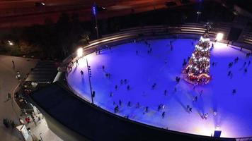 People ice skate around a Christmas tree in a skating rink at night with light show