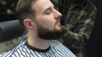 barbeiro usou secador de cabelo e escova redonda para modelar e estilizar a barba do homem após o barbear video