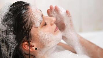 mujer joven en baño de burbujas se ríe y acaricia burbujas en la cara video