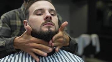 Barber rubs beard oil and shapes man's facial hair with hands video