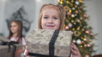 deux jeunes filles rient et jouent avec des cadeaux emballés devant un arbre décoré video