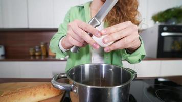 Young woman holds knife and cracks egg into large pot in kitchen video