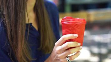 close-up em uma xícara de café vermelha segurada por uma mulher morena falando