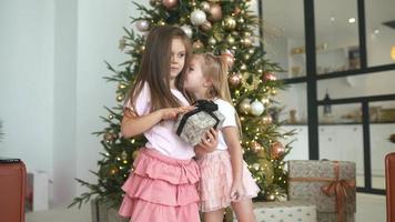 Two young girls laugh and play with wrapped gifts in front of a decorated tree video