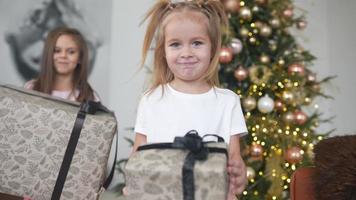 Two young girls laugh and play with wrapped gifts in front of a decorated tree video