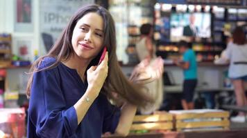 Young brunette woman smiles and combs fingers through hair while holding a phone to her ear video