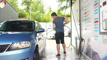 Young man in a tee shirt and shorts washes a car