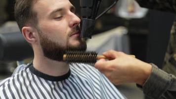Barber used hair dryer and round brush to shape and style man's beard after a shave video