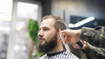 Barber trims hair of male client with comb and clippers video