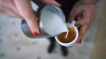 Feminine hands with red nails pour steamed milk into a cup of espresso shots creating latte art video