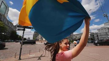 mujer joven lleva la bandera ucraniana soplando en el viento en la calle en un hermoso día video