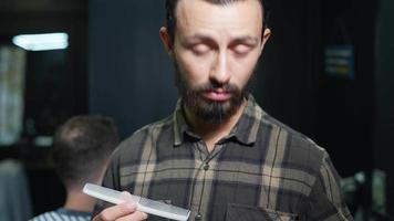 barbeiro masculino enfrenta a câmera fazendo contato visual na loja com o cliente em segundo plano