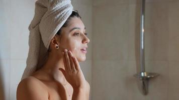 mujer con cabello en toalla suaviza la crema hidratante en la cara después de la ducha video