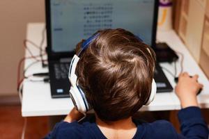 vista trasera del niño con auriculares usando la computadora en casa. foto