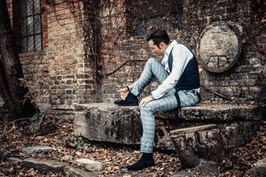 Retro-styled man cleaning shoes while sitting outdoors. photo