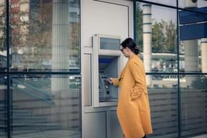 Young businesswoman using cash machine in front of bank. photo