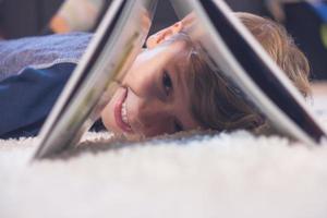 Happy kid having fun while peeking through book and looking at camera photo