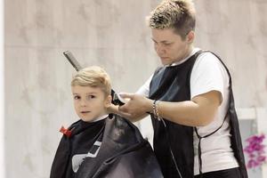 niño lindo cortándose el pelo en la peluquería. foto