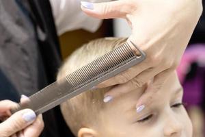 primer plano del peluquero peinando el cabello del niño en el salón. foto