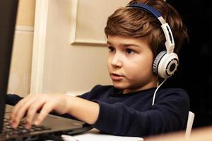 Cute kid with headphones playing online games on laptop. photo