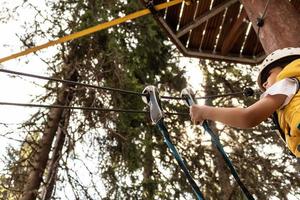 Below view of kid attaching safety harness on a rope during canopy tour in the forest. photo