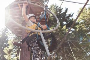 Low angle view of kid crossing obstacles while zip lining in nature. photo