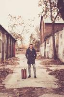 Man in coat with vintage suitcase standing amidst ruined buildings. photo