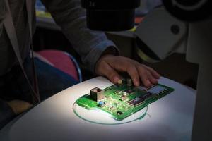 Close up of IT student examining mother board part under microscope. photo