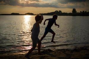 chicos felices corriendo en la playa al atardecer. foto