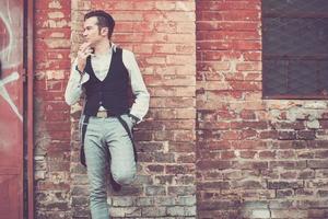 Pensive man leaning on a wall and smoking a cigarette. photo