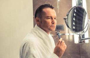 Man in bathrobe shaving with razor in the morning. photo