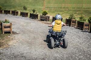 Back view of child driving quadricycle on dirt road. photo