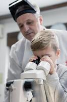 Little boy looking through microscope with help of a teacher. photo