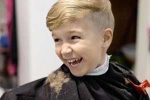 Happy boy having fun during haircut at barber shop. photo