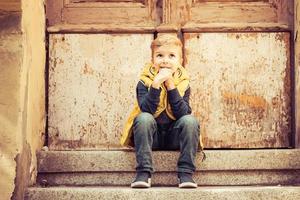 lindo niño sentado en los escalones y pensando en algo. foto