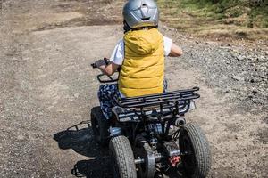 Back view of child driving quadricycle on dirt road in nature. photo