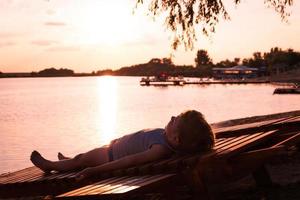 Small boy relaxing on deck chair by the water at sunset. photo