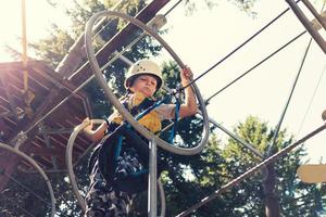 Below view of boy crossing obstacles while zip lining in the forest. photo