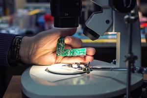 Close up of IT technician examining computer part under microscope photo