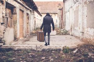 Back view of man carrying suitcase and walking away. photo